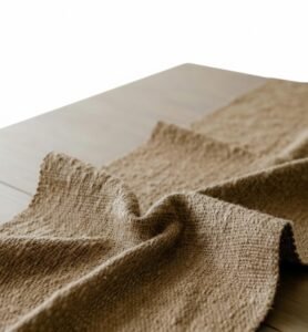 Close-up of a textured brown burlap fabric runner draped over a wooden surface.