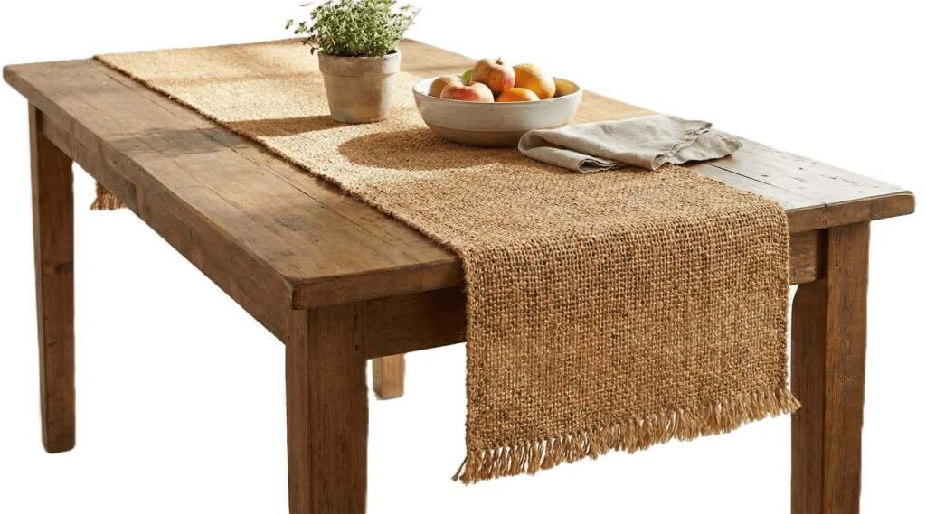 Rustic burlap jute table runner with fringe on a wooden dining table with fruit and plants.