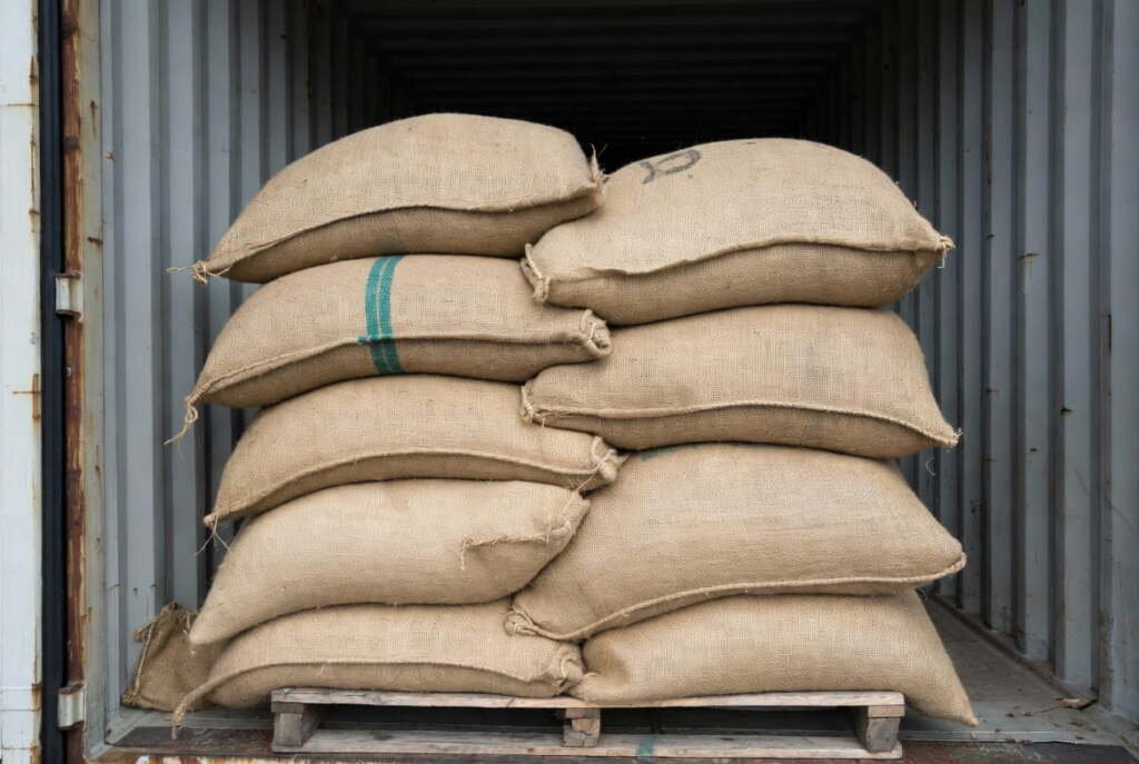 bulk burlap sacks shipping container Large burlap sacks of agricultural goods stacked on a pallet inside a metal shipping container for export.