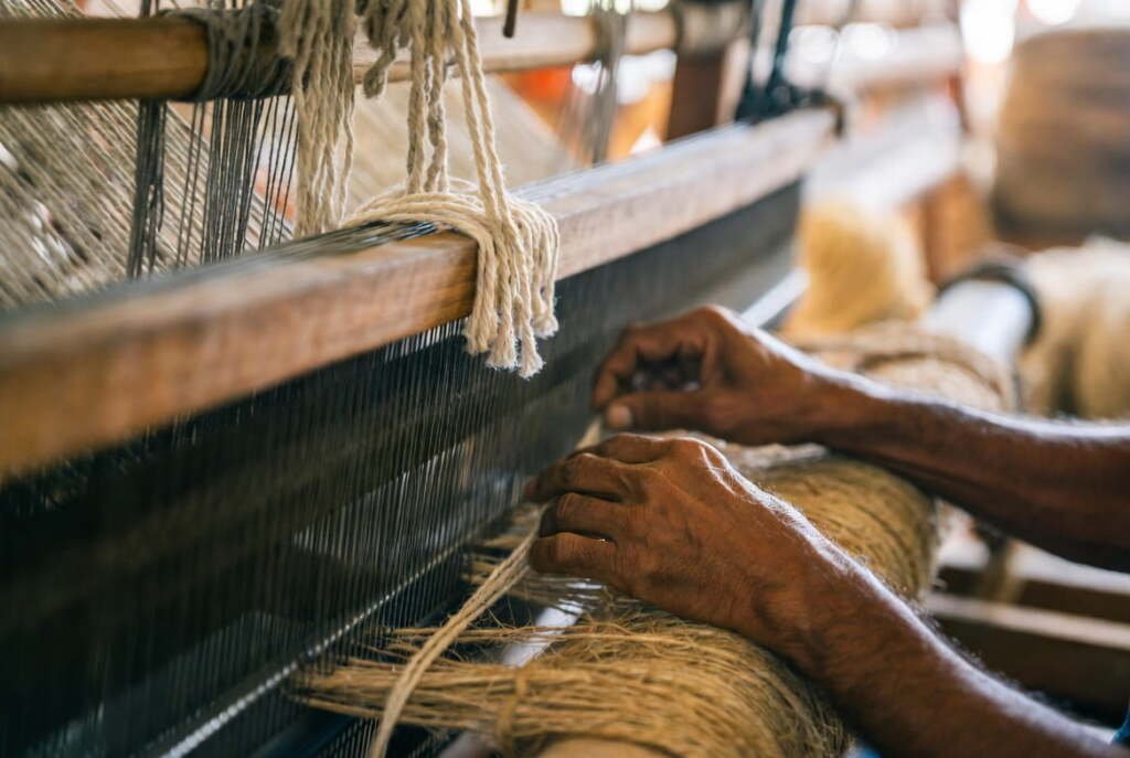 artisan weaving a handmade jute and cotton rug on a traditional wooden handloom, authentic craft detail.