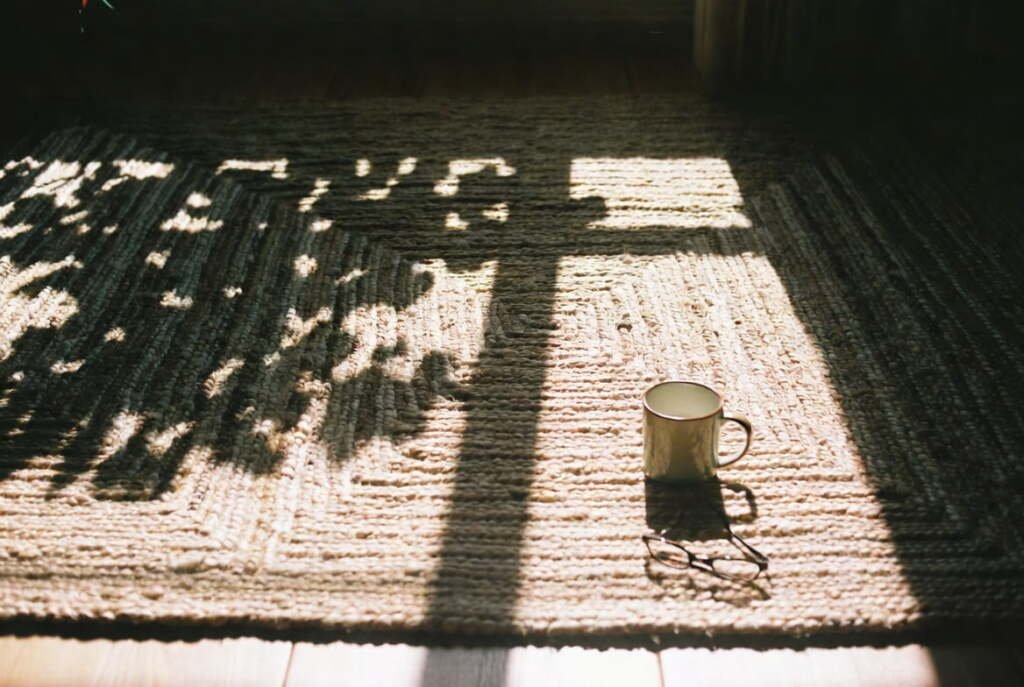 natural sunlight and window shadows on a textured handmade rug with a mug, creating a peaceful home atmosphere.