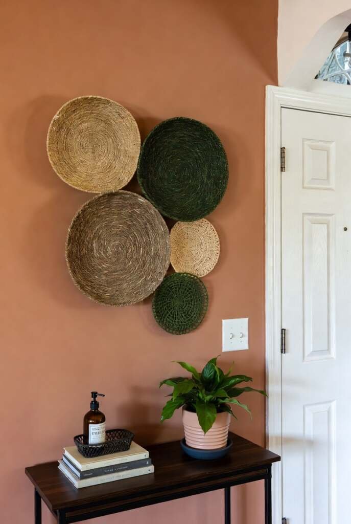 wall basket decor Gallery wall of various sized woven decorative baskets in natural and green tones on a terracotta-colored wall.