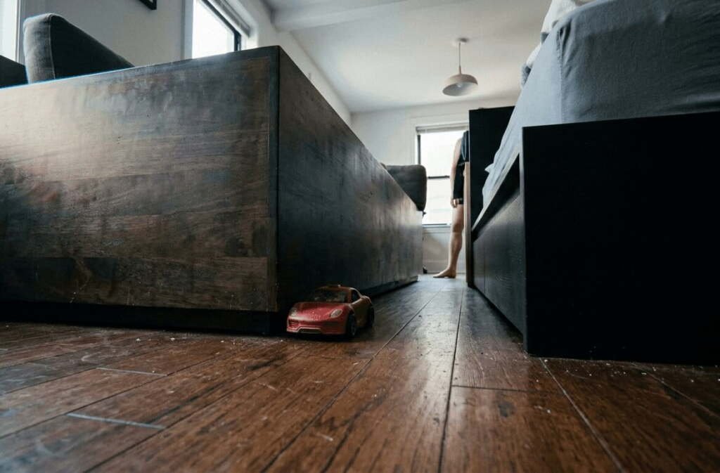 Floor-level view of boxy platform sofa and bed frame with no leg clearance, a toy car trapped against the solid base