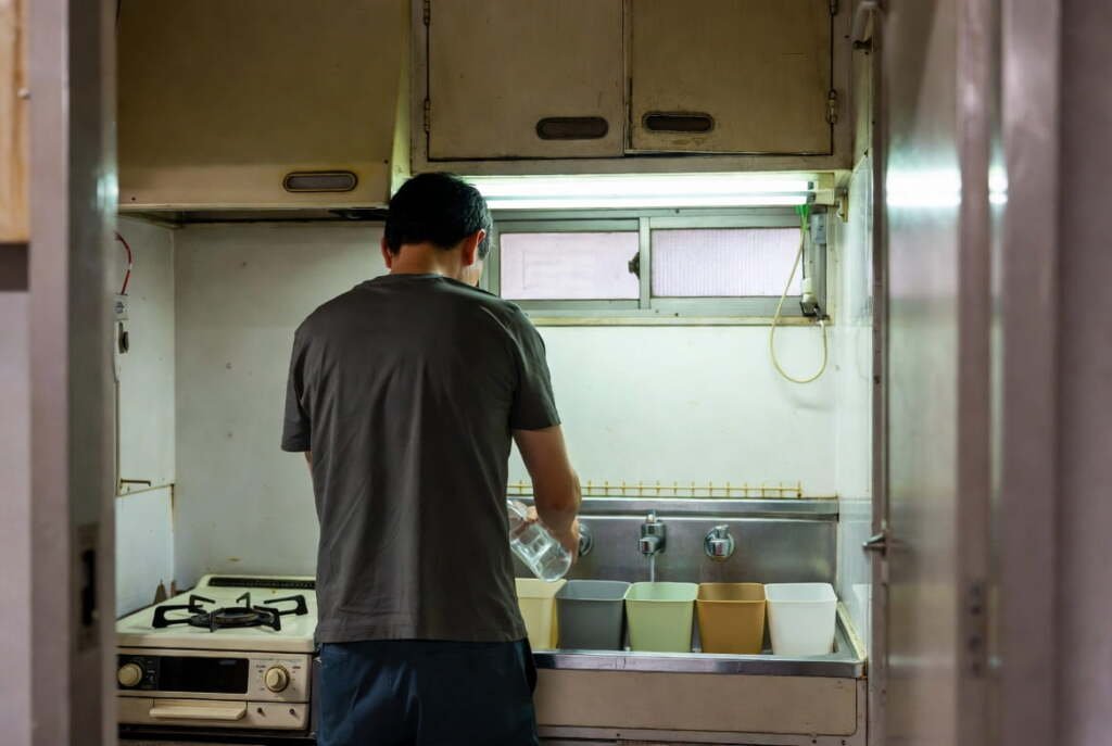 Man sorting recyclables in a compact Japanese minimalist home kitchen — mottainai sustainable living in action