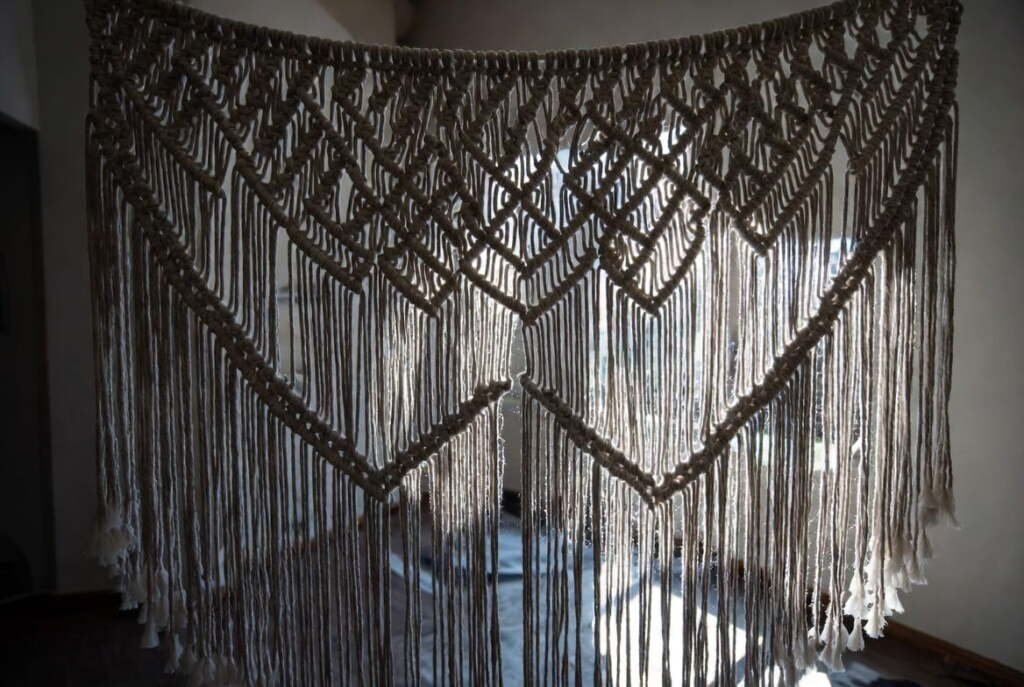 large-jute-macrame-wall-art-sunlight-uv-exposure Large jute macrame wall hanging backlit by direct sunlight showing UV exposure risk to natural fiber wall decor.