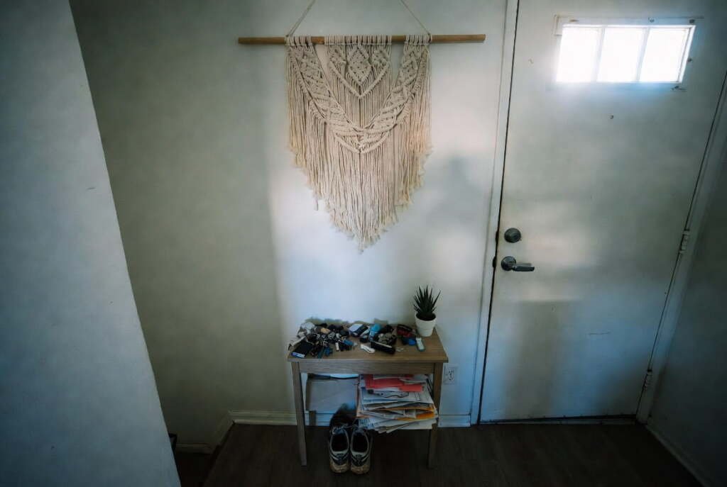 macrame-wall-decor-entryway-above-console-table Large macrame wall hanging mounted high in a home entryway above a wooden console table near the front door.