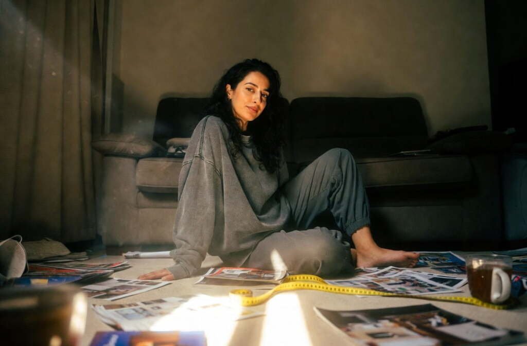 Woman sitting on floor surrounded by magazines and a measuring tape while decorating small spaces in her apartment